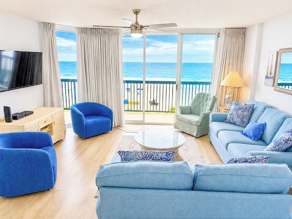 A living room with a view of the ocean, a ceiling fan, and a flat-screen TV.