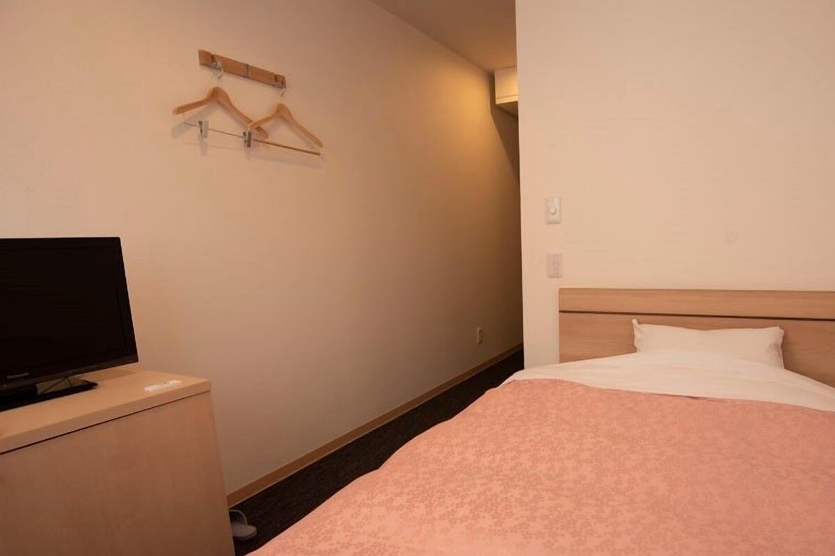Una habitación de hotel con una cama, un televisor sobre un mueble bajo y un perchero en la pared.