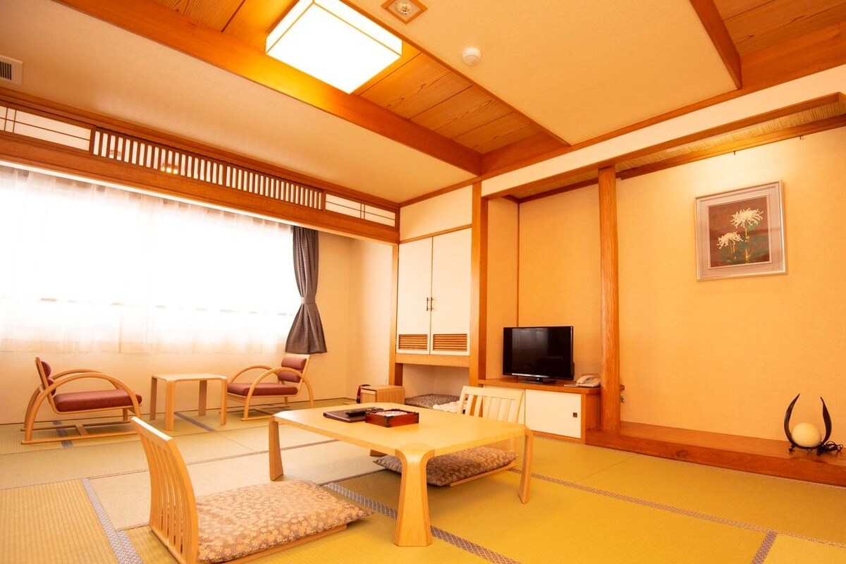 A traditional Japanese-style room with tatami flooring, a low table with cushions, a television, and a cabinet.