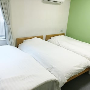 Una cama individual con ropa de cama blanca en una habitación con pared verde y ventana con cortinas.