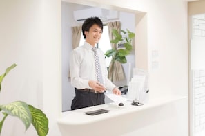 A person standing at a reception desk in a hotel lobby with a plant and a window in the background.