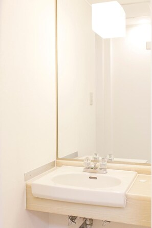 A bathroom with a white sink, a mirror, and a light fixture above the mirror.