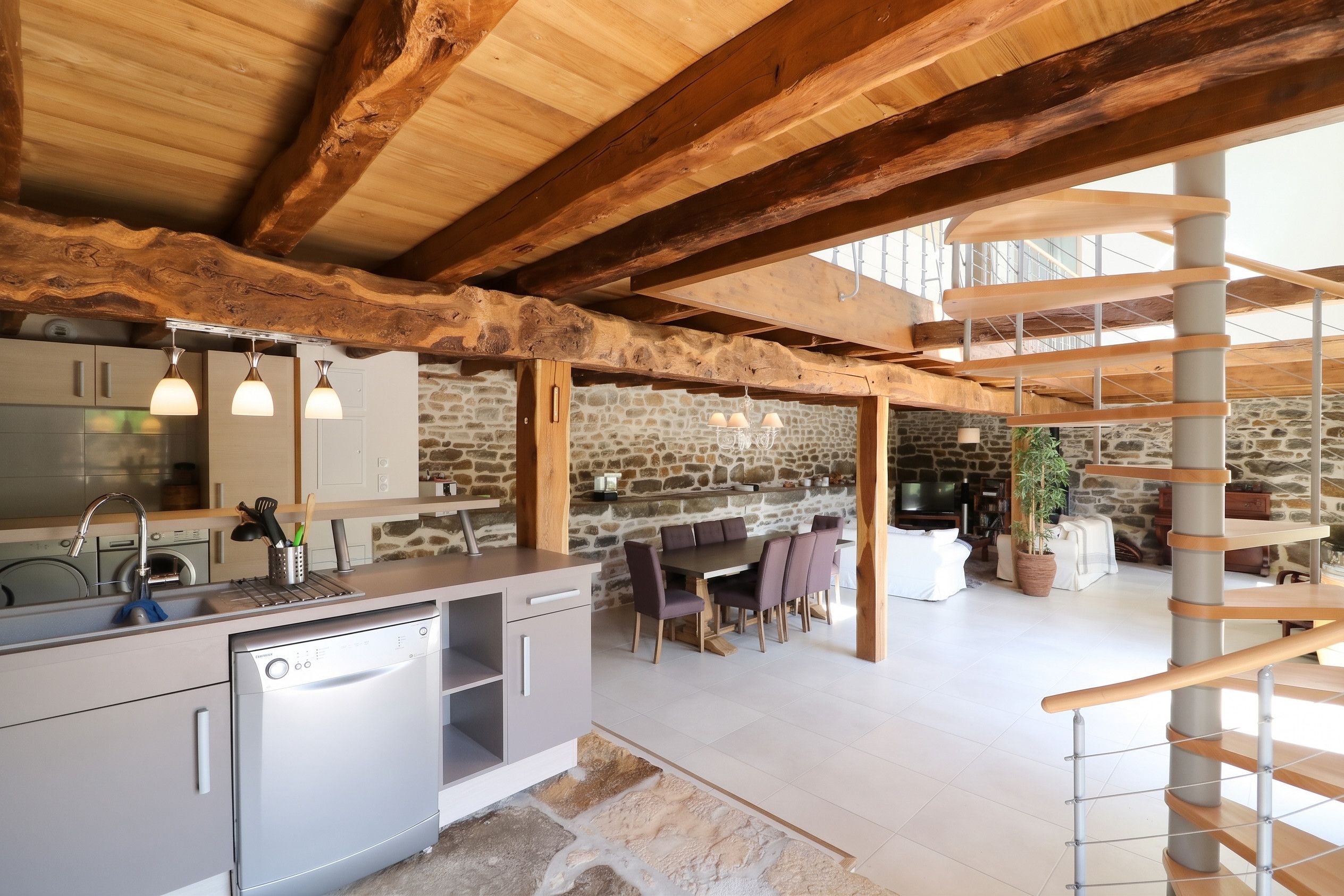 Une cuisine moderne dotée d’appareils électroménagers intégrés, un coin repas agrémenté d’un mur en pierre et un escalier en colimaçon.