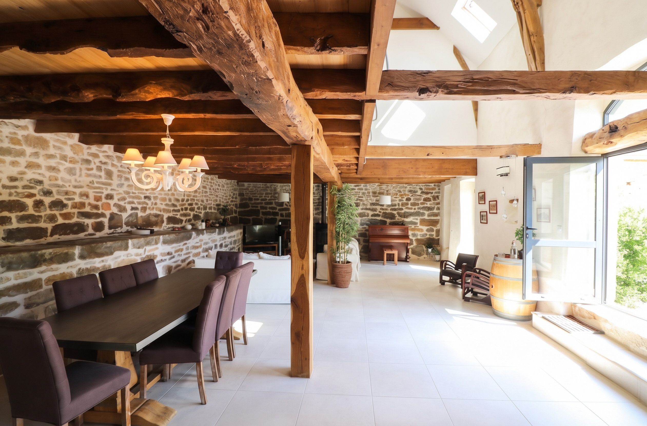 Un interior rústico con vigas de madera a la vista, una pared de piedra, un comedor con una mesa larga y sillas, y un piano.