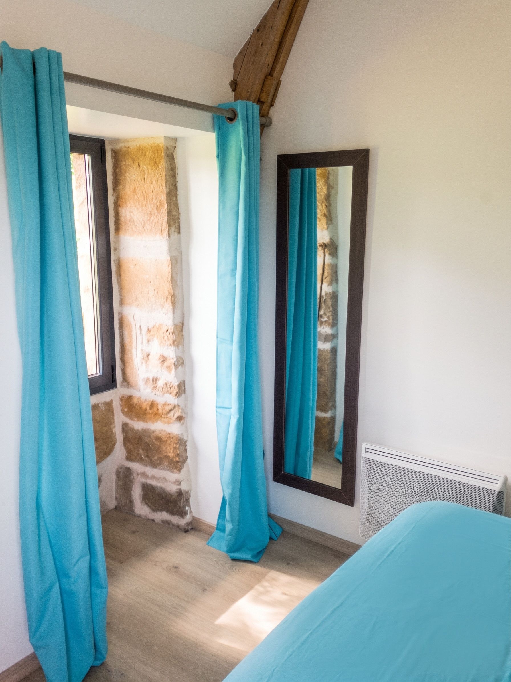 A room with a bed, a window with curtains, a stone wall, and a radiator.