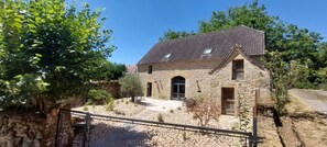 A stone house with a tiled roof, a front door, and a small garden area with a gravel path. - Homerez - House in Thégra. (Thégra)