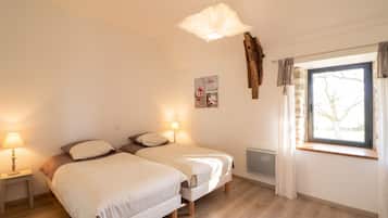 Ein Schlafzimmer mit zwei Betten, einem fensterbelaubten Fenster, einer Pendelleuchte und einer Heizkörper.