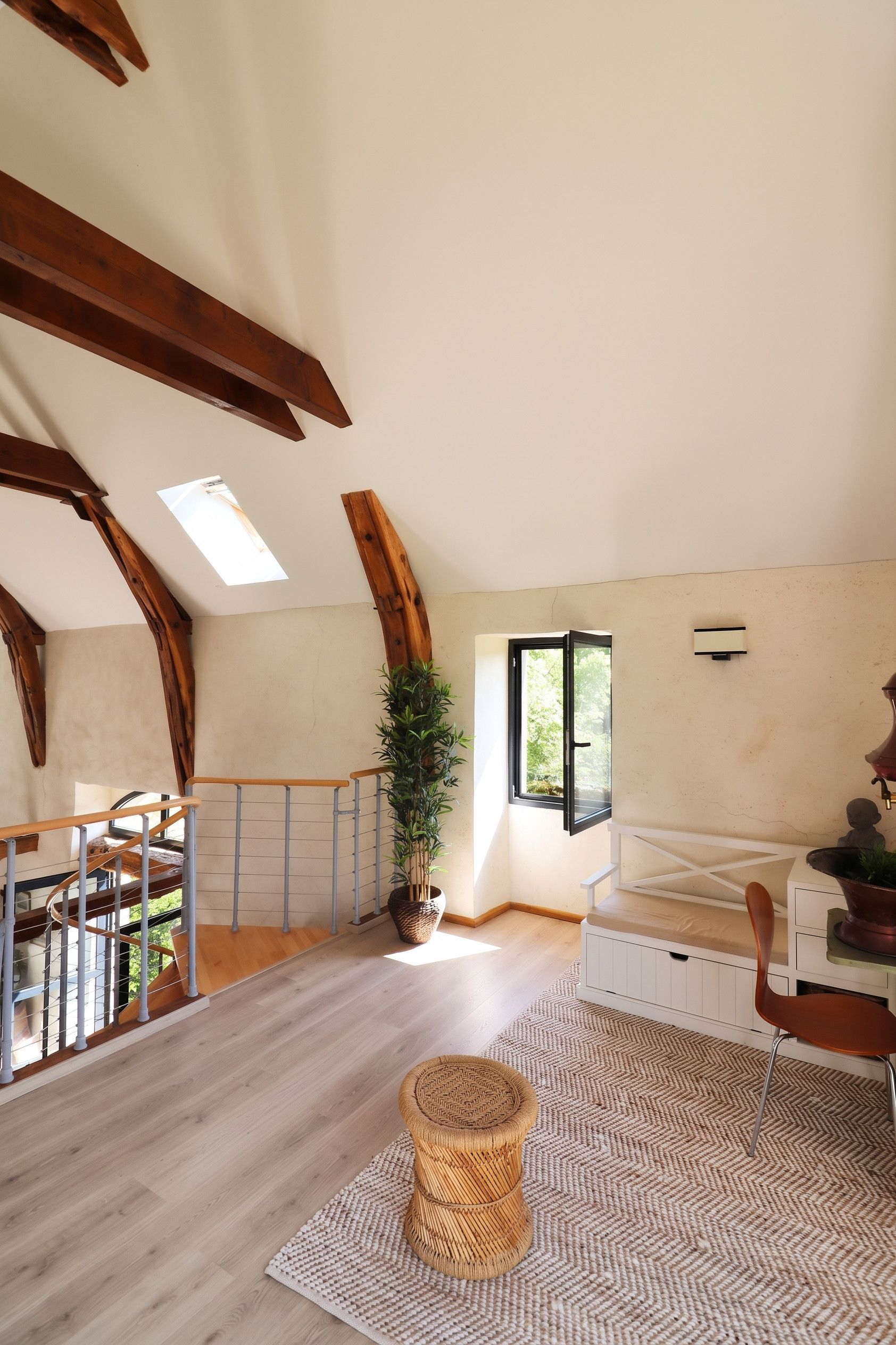 Ruime loft slaapkamer met schuine plafonds, houten balken, een groot raam en uitzicht op groen.