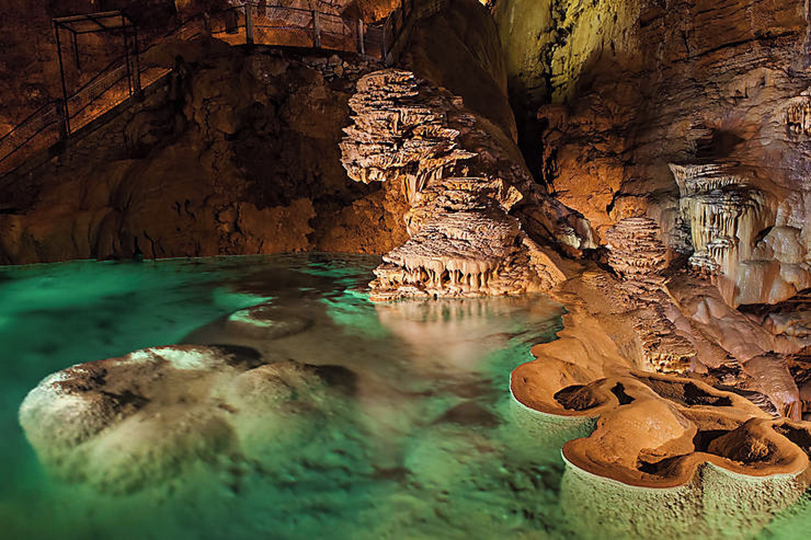 Una cueva con estalactitas y estalagmitas, un estanque de agua y una escalera de metal.