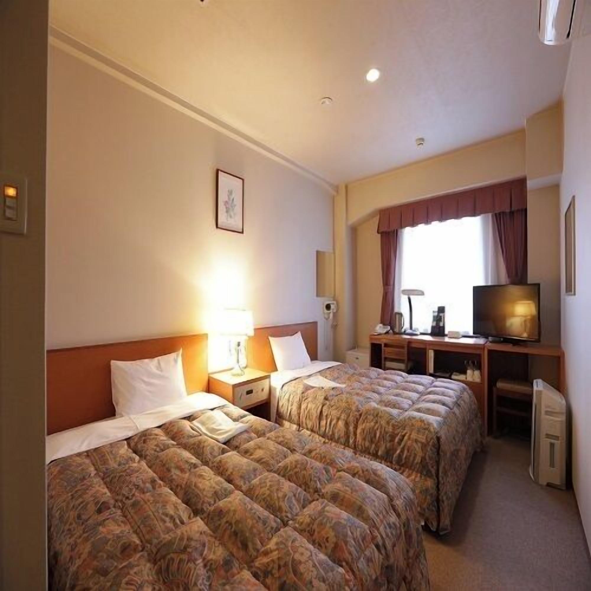 Een hotelkamer met twee bedden, een bureau met een televisie en een raam met gordijnen.