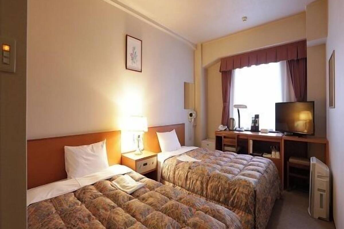 Een hotelkamer met twee bedden, een bureau met een televisie en een raam met gordijnen.