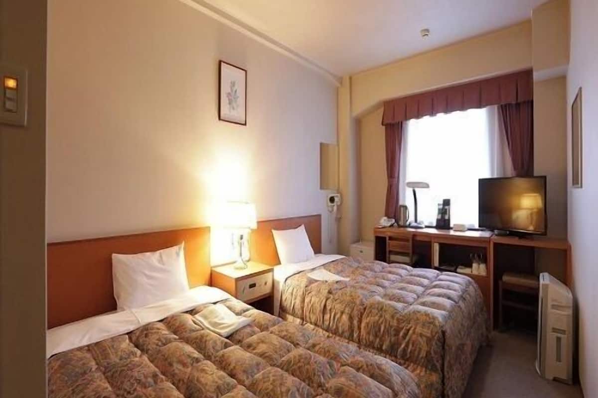 A hotel room with two beds, a desk with a television, and a window with curtains.