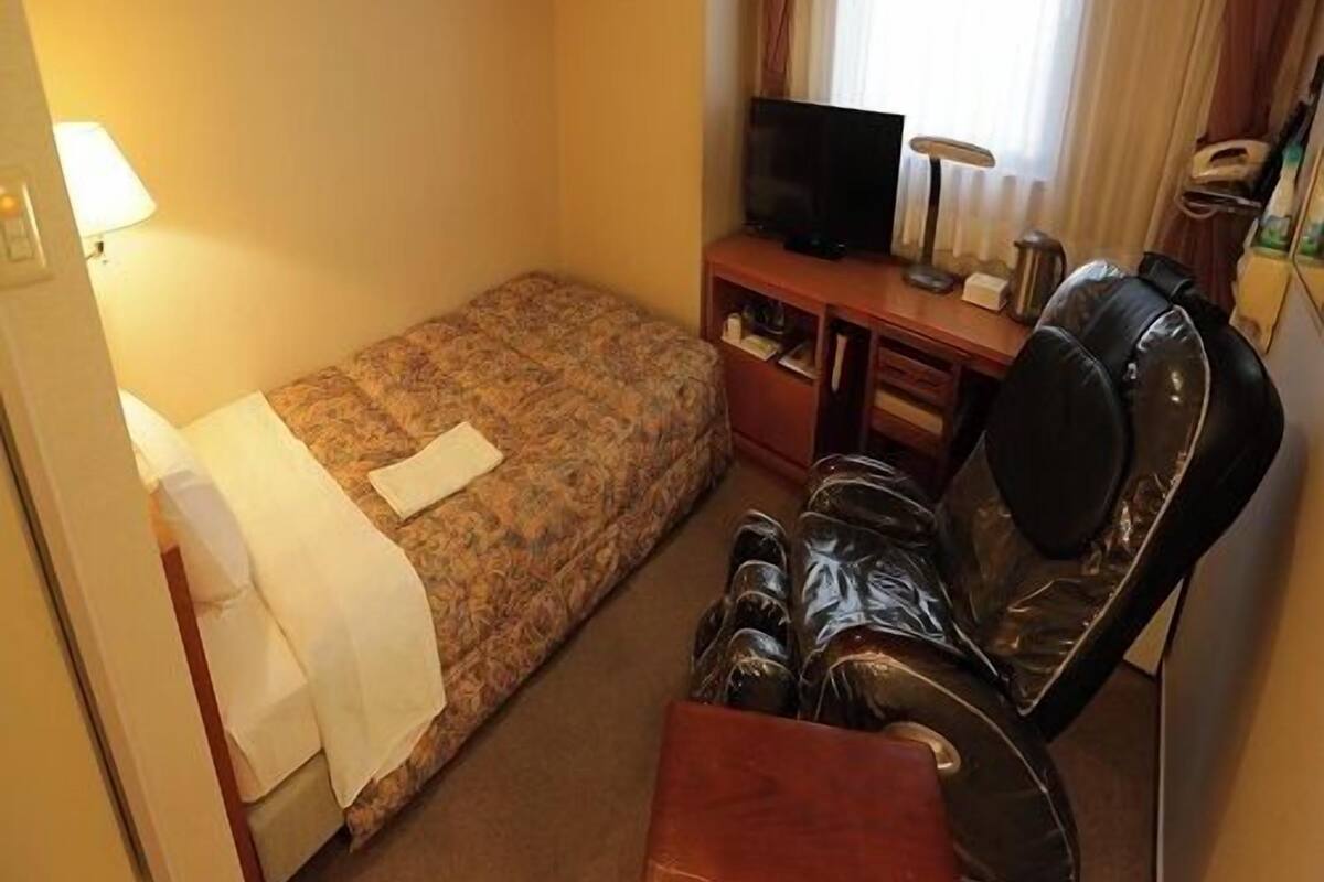 Een compacte hotelkamer met een bed, een bureau met televisie, een stoel en een klein tafeltje.