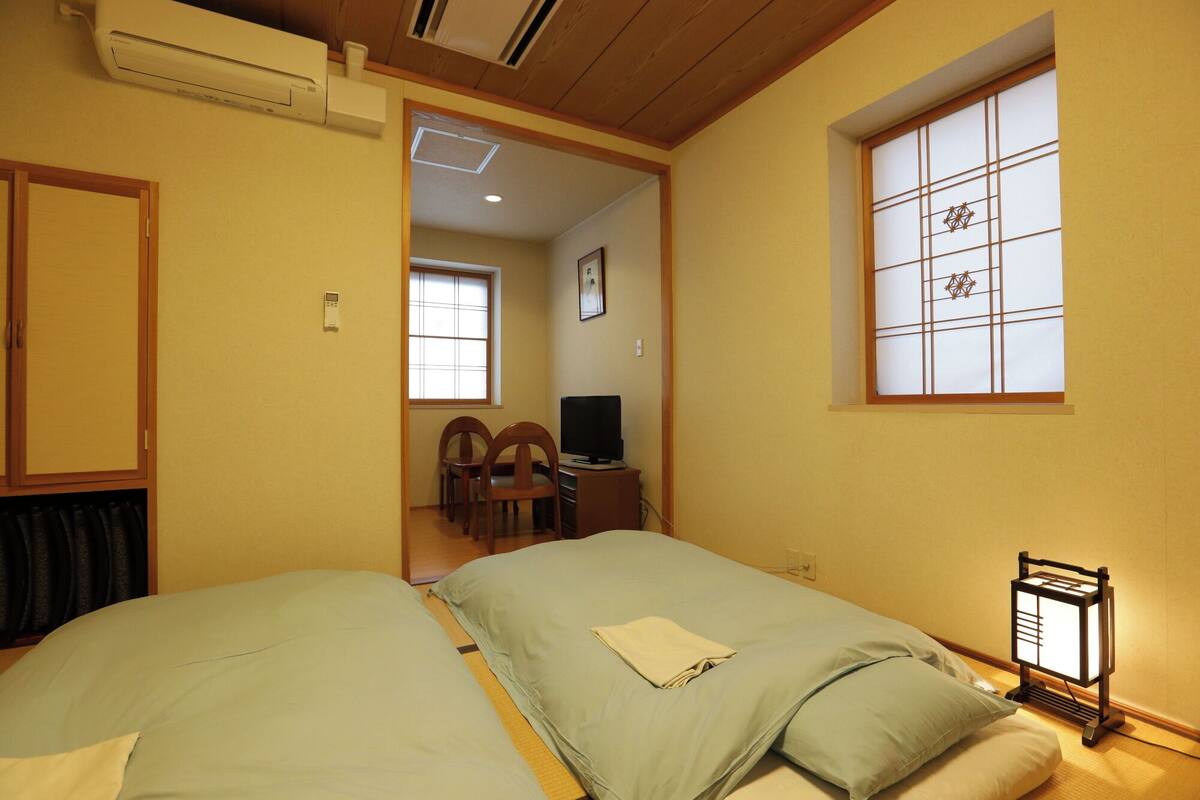 Een hotelkamer met twee bedden, een televisie, een bureau en een traditioneel Japans raam.