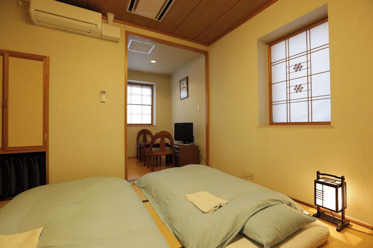 A hotel room with two beds, a TV, a desk, and a traditional Japanese window.