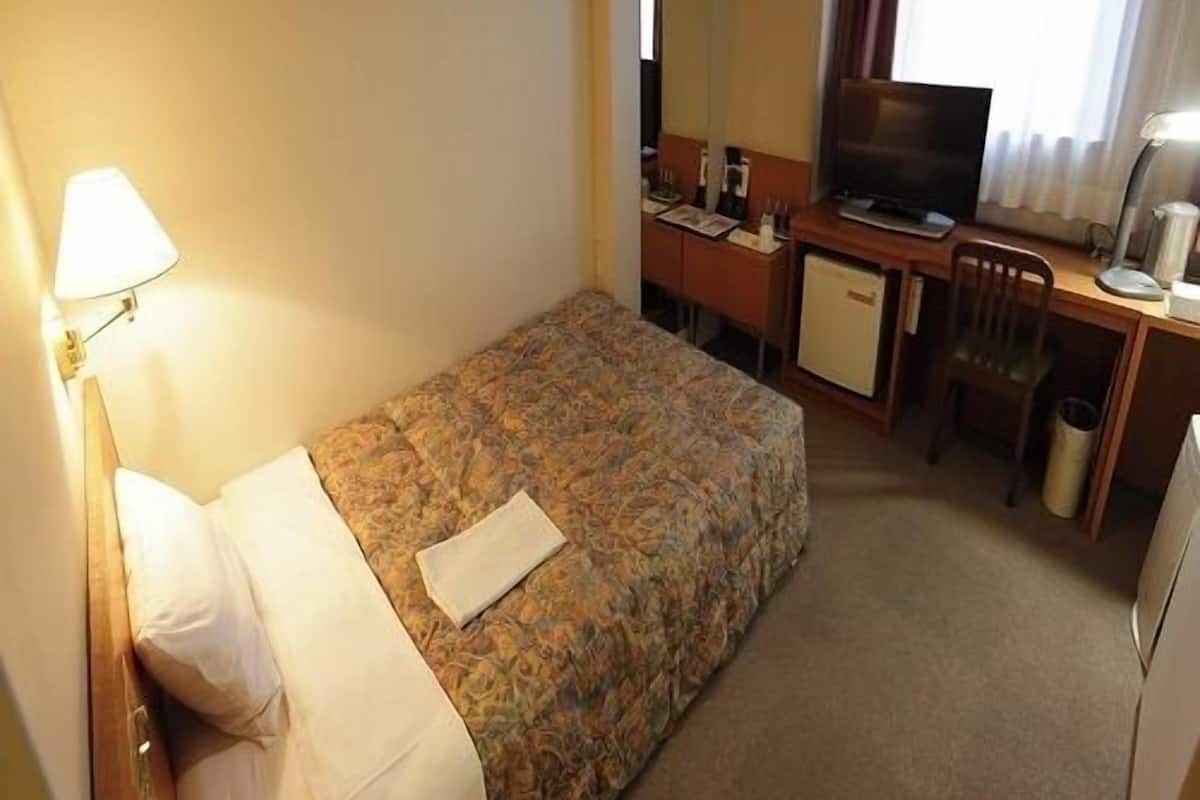 A hotel room with a bed, a desk, a television, and a lamp.
