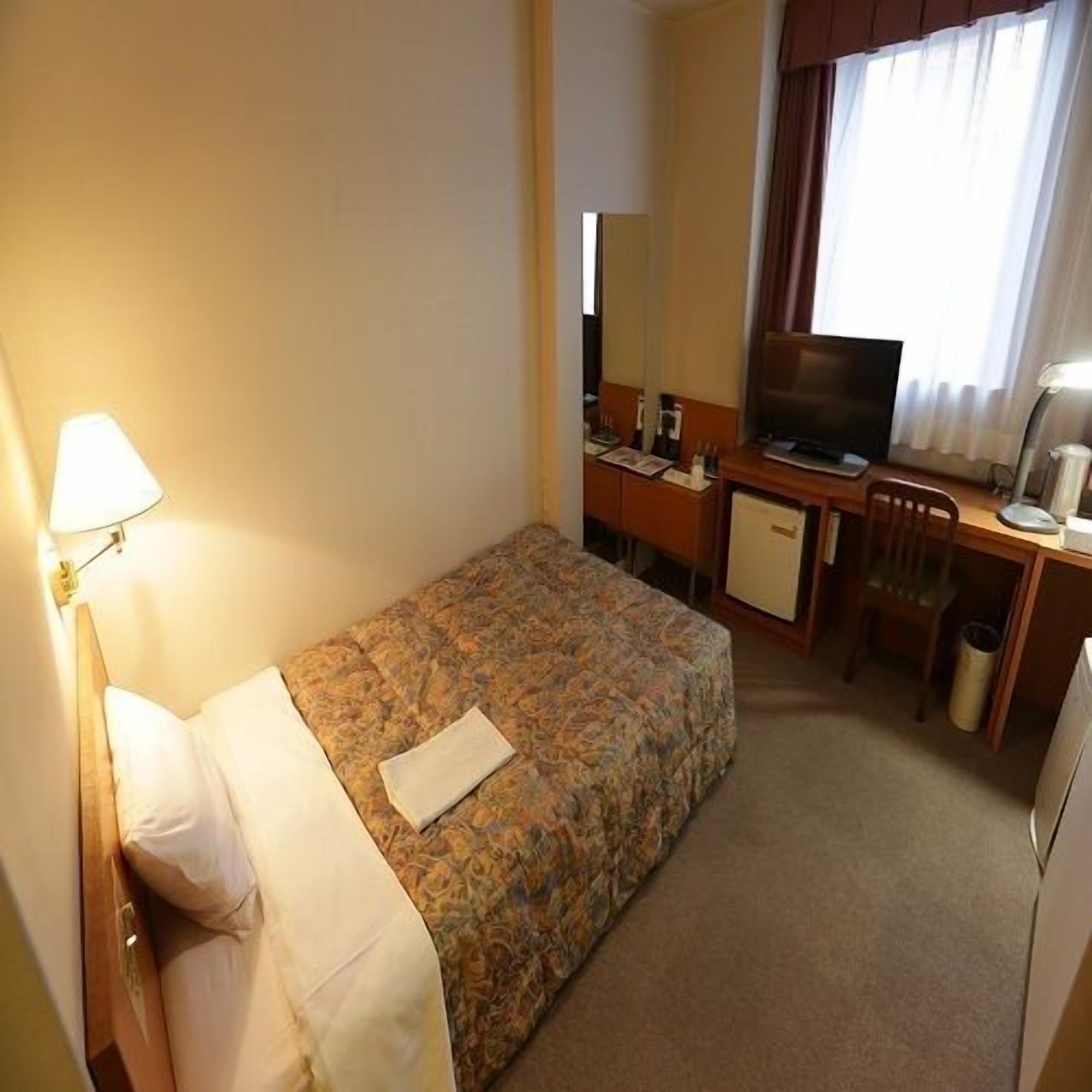 Een hotelkamer met een bed, een bureau, een televisietoestel en een lamp.