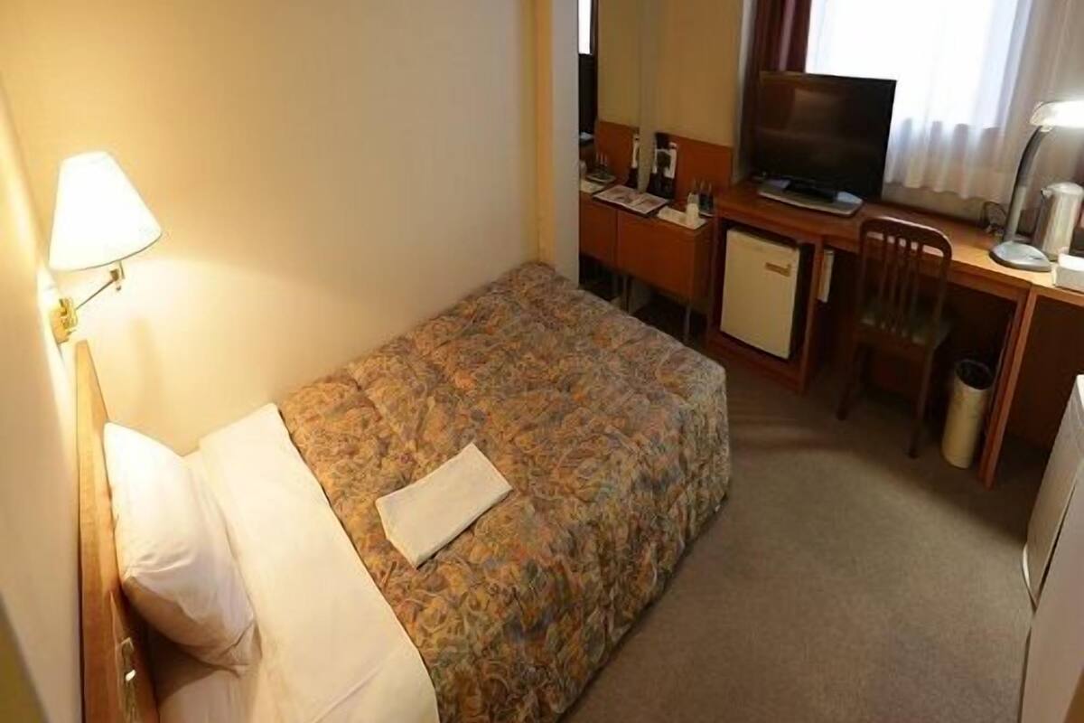 Een hotelkamer met een bed, een bureau, een televisietoestel en een lamp.