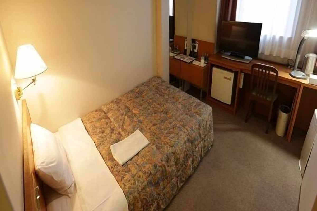 Ein Hotelzimmer mit Bett, Schreibtisch, Fernseher und Lampe.