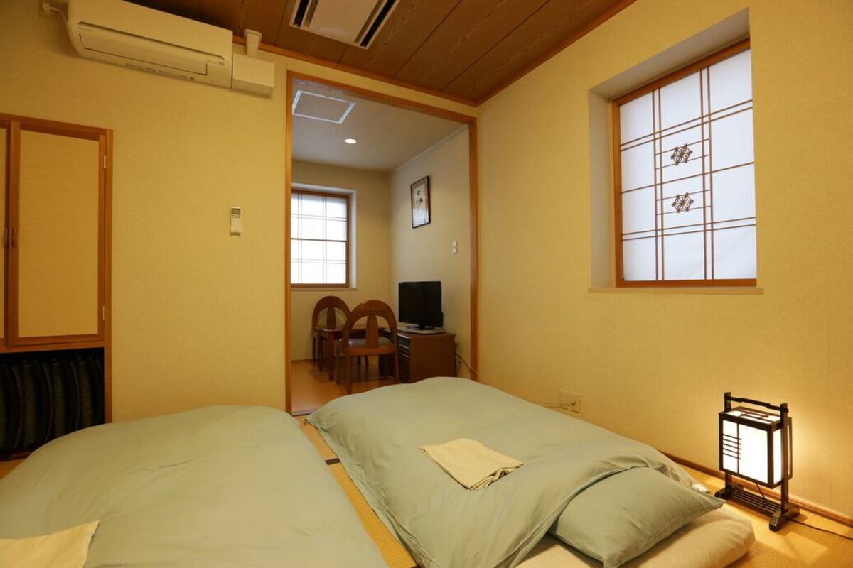 Een hotelkamer met twee bedden, een bureau met een computer, een stoel en een traditioneel Japans raam.