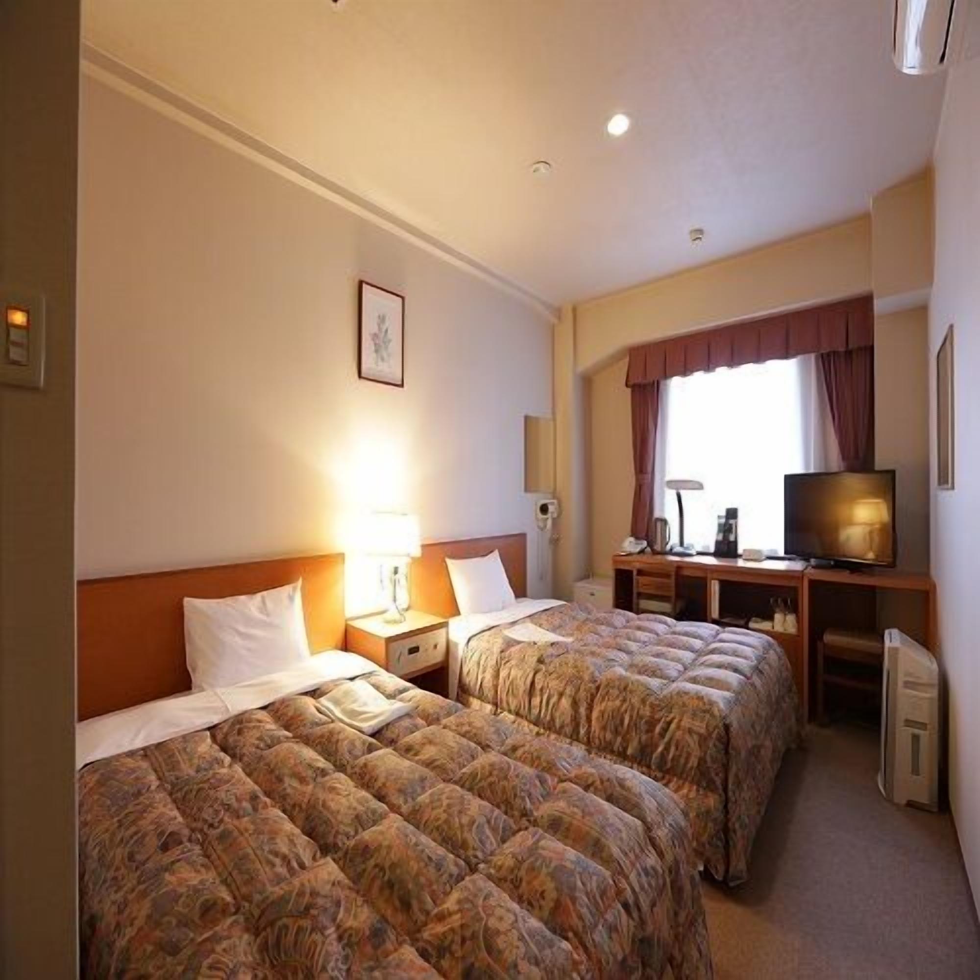 Een hotelkamer met twee bedden, een bureau, een televisie en een raam met gordijnen.