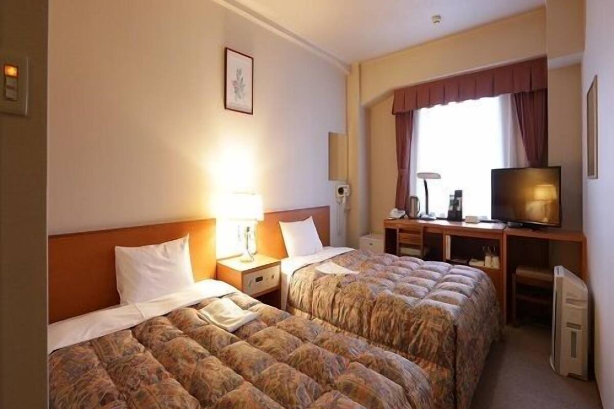 Een hotelkamer met twee bedden, een bureau, een televisie en een raam met gordijnen.