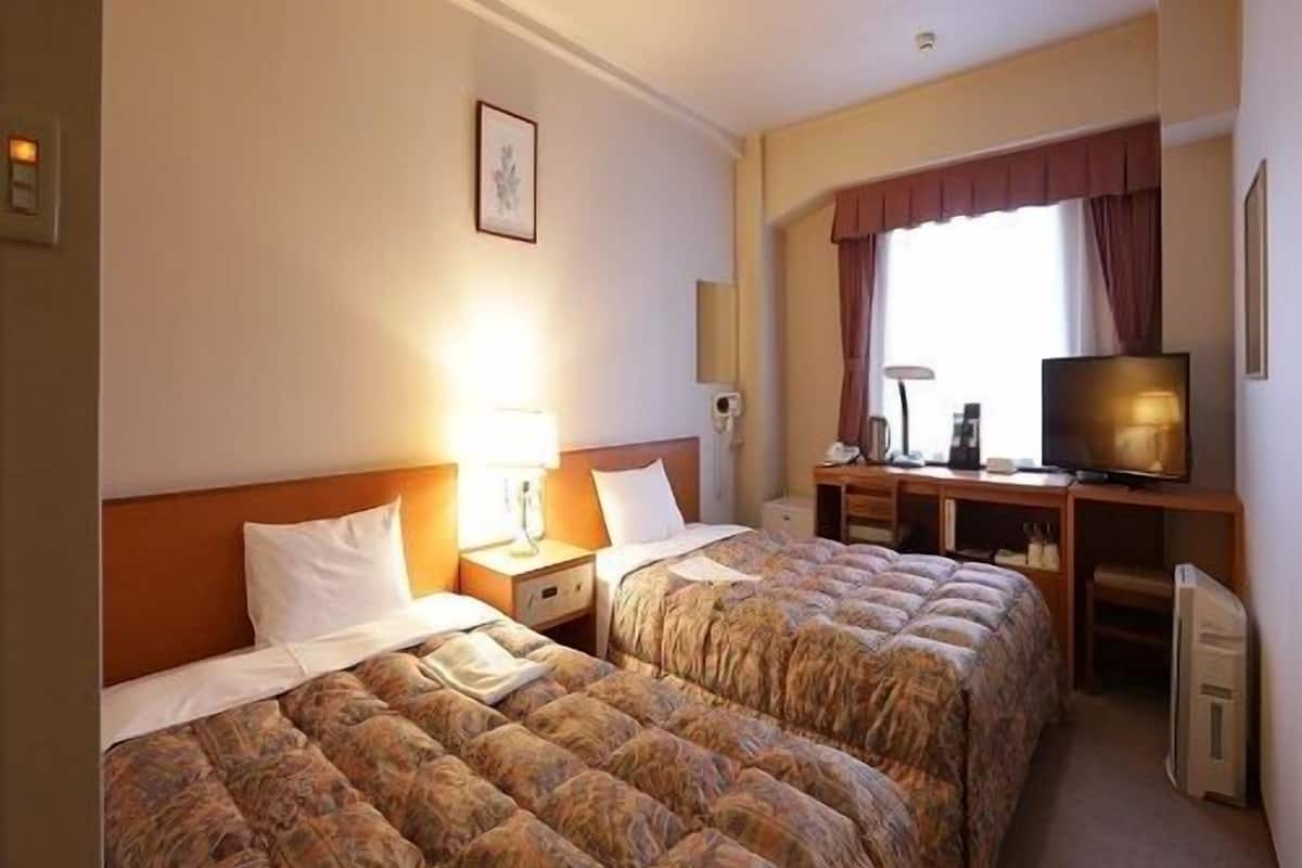 Ein Hotelzimmer mit zwei Betten, einem Schreibtisch, einem Fernseher und einem fenster mit Vorhängen.