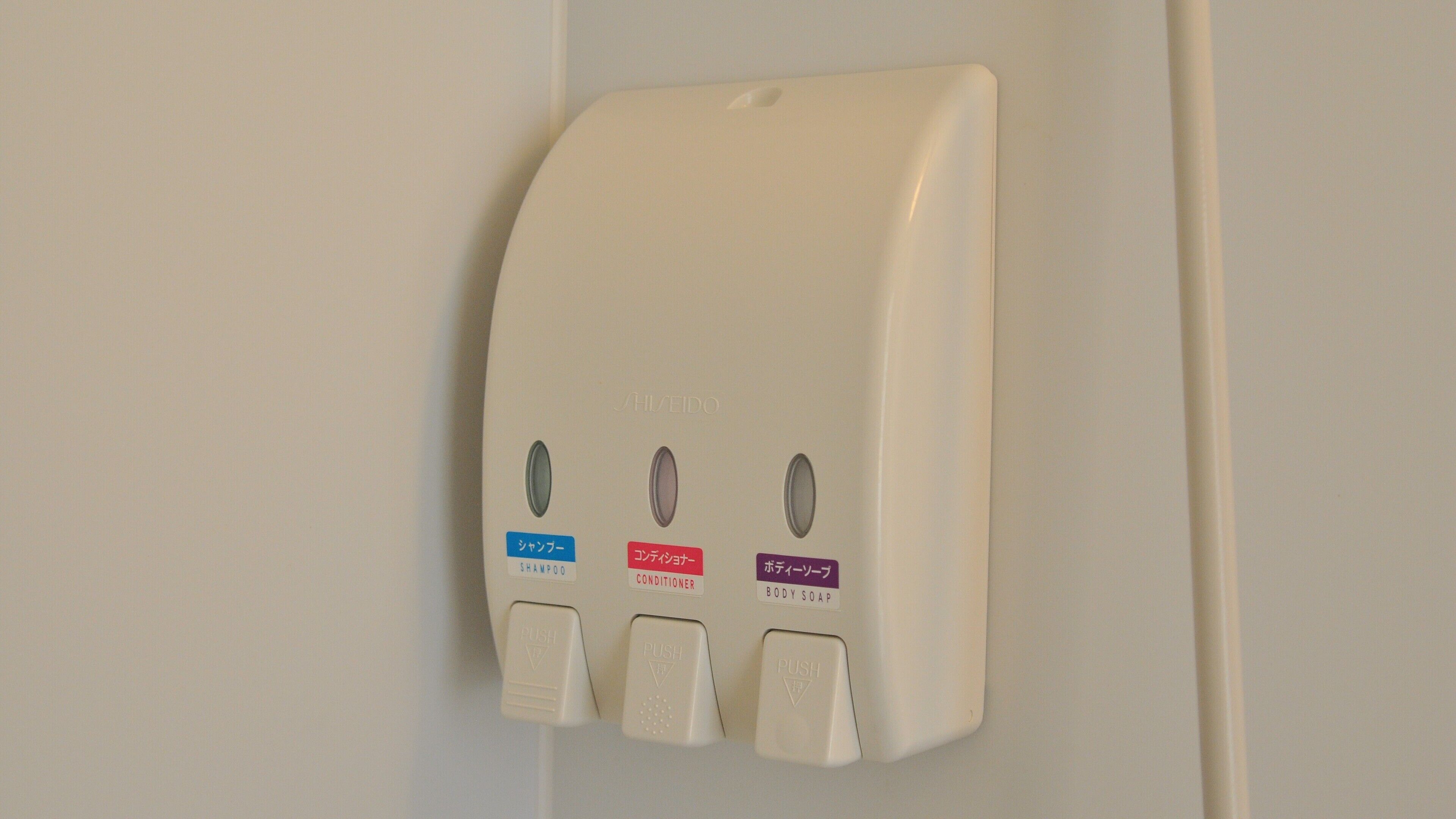 A wall-mounted dispenser with three buttons labeled for shampoo, conditioner, and body soap.