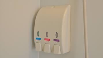 A wall-mounted dispenser with three buttons labeled for shampoo, conditioner, and body soap.