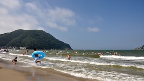 Ein Strand mit badenden und surfenden Menschen, ein Berg im Hintergrund und ein klarer Himmel.