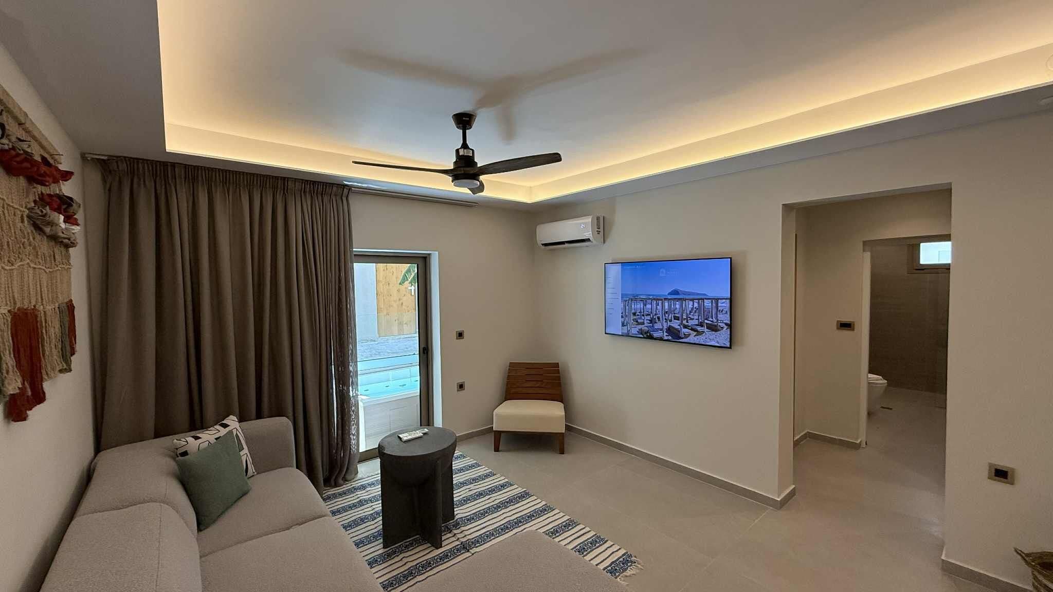Una sala de estar moderna con un sofá, una mesa de centro, un televisor montado en la pared y un ventilador de techo.