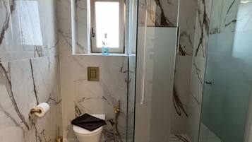 Un baño moderno con cabina de ducha de vidrio, paredes de mármol, un inodoro y un lavabo.