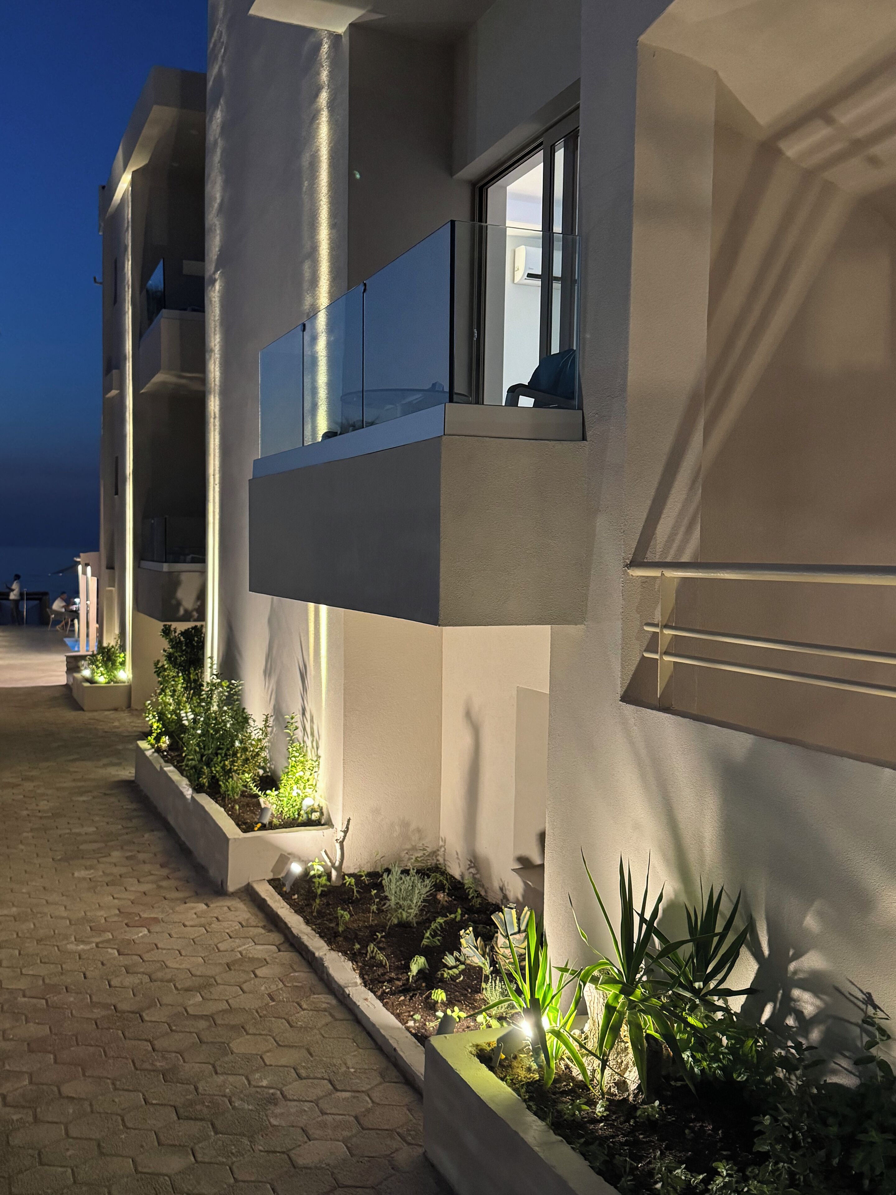 Un edificio moderno con fachada plana, amplias ventanas y un área de entrada bien iluminada con plantas en macetas.