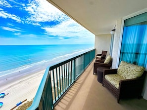 A balcony with a view of the beach and ocean, furnished with wicker chairs and a sofa. - Ashworth 1506 (North Myrtle Beach)