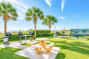 A park with a picnic table and benches, surrounded by palm trees and a view of the ocean.