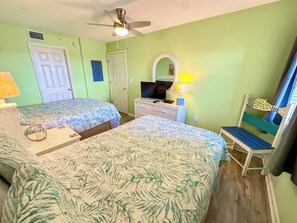 Una habitación con dos camas, televisi ón, escritorio con lámpara y una silla.