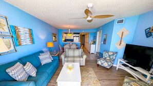 A living room with a blue couch, striped chairs, a coffee table, and a TV on a stand.