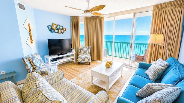 A living room with a TV, two sofas, a coffee table, and a balcony with a view of the sea.