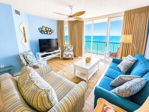 A living room with a TV, two sofas, a coffee table, and a balcony with a view of the sea.