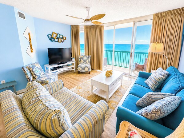 Un salón con televisor, dos sofás, una mesita de centro y un balcón con vistas al mar.