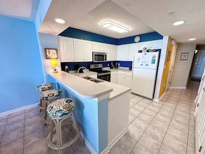 A kitchen with white cabinets, a microwave, a refrigerator, and a bar stool area.