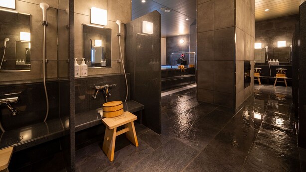 Ein modernes Badezimmer mit dunklen Fliesen, mehreren Waschbecken und Spiegeln.