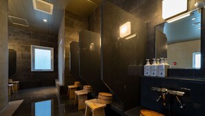 Ein modernes Badezimmer mit dunklen Steinwänden, Holzschemeln und einer Holzbank sowie einem großen Spiegel.