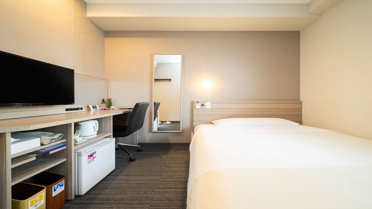 Hotelkamer met een bed, een bureau met een televisie, een minibar, een prullenbak en een spiegel.