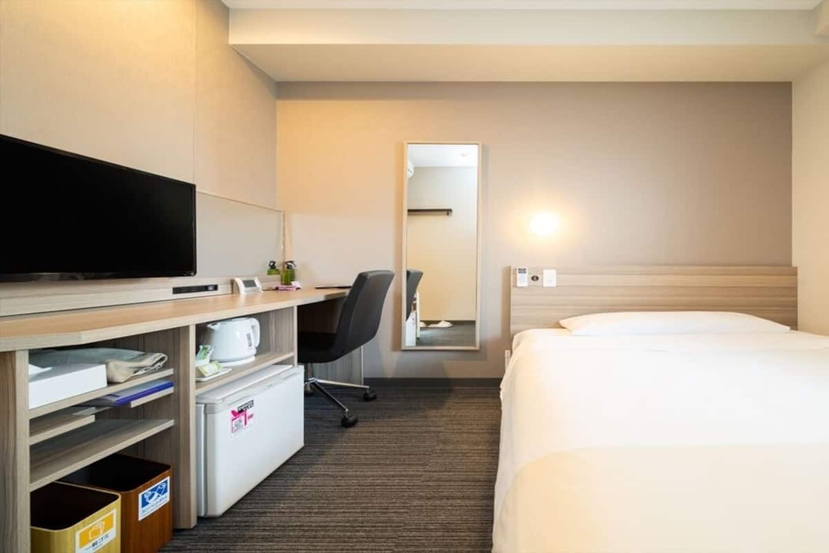 Une chambre d’hôtel comprenant un lit, un bureau avec une télévision, un mini-réfrigérateur, une poubelle et un miroir.