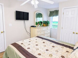 Un dormitorio con cama, cómoda, televisor montado en la pared y ventana con cortinas.
