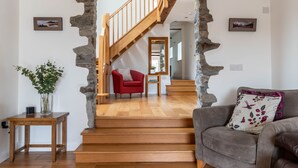 A staircase with wooden steps and stone accents, leading to a red chair and a grey sofa in a well-lit room with wooden flooring. - Bryn Eithin Cottage Far From the Madding Crowd (Corwen)