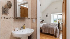 A bathroom with a sink, mirror, and towel rack. The room has a wooden floor and a bed with a view of the outdoors. - Bryn Eithin Cottage Far From the Madding Crowd (Corwen)