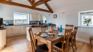 A modern kitchen with wooden beams, white cabinets, and a dining area with a wooden table and chairs. - Bryn Eithin Cottage Far From the Madding Crowd (Corwen)
