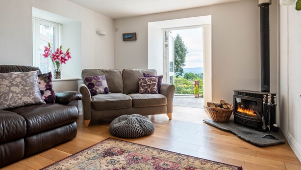 A cozy living room with a fireplace, a sofa, a loveseat, and a rug. - Bryn Eithin Cottage Far From the Madding Crowd (Corwen)